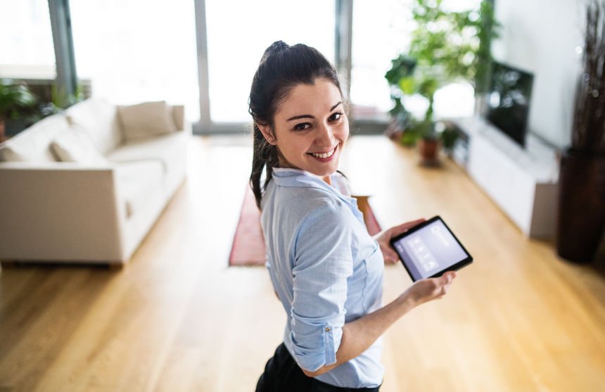 A woman holding a tablet with smart home screen at home.
