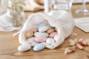 Pochon en tissu blanc rempli de dragées pastel sur une table en bois pour calculer combien de dragées par personne.